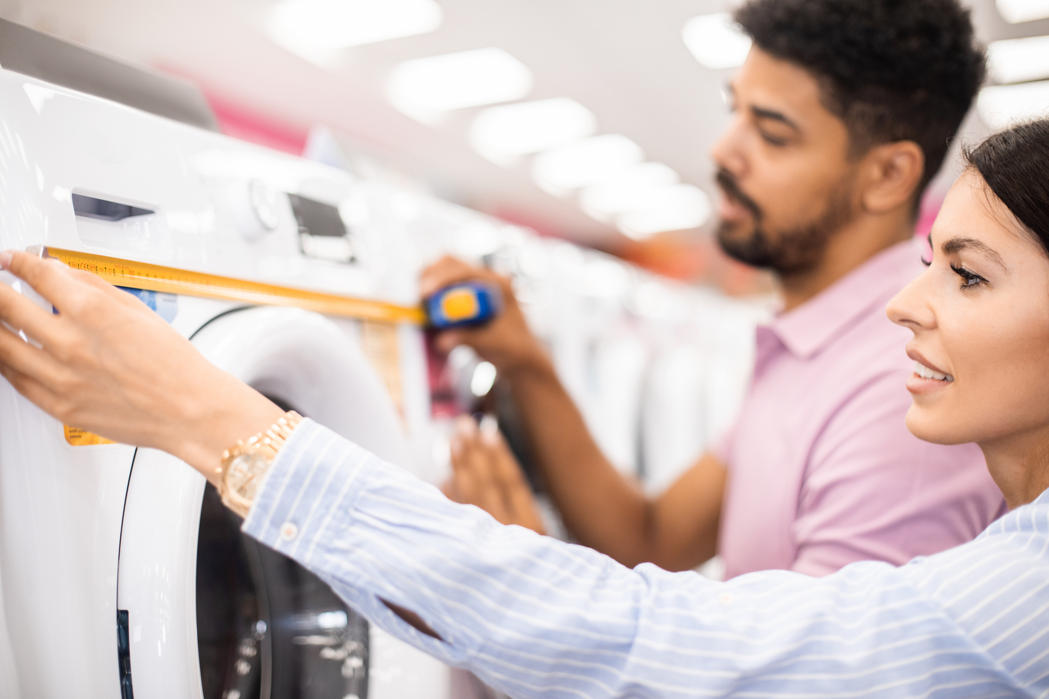 A man and a woman measuring a front load washer